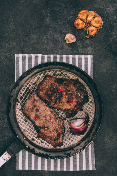 top view of gourmet roasted steaks on frying pan and grilled garlic on black