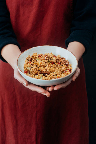 cropped image of female cook holding bowl with granola