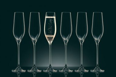 five empty glasses and one glass with champagne on black clipart