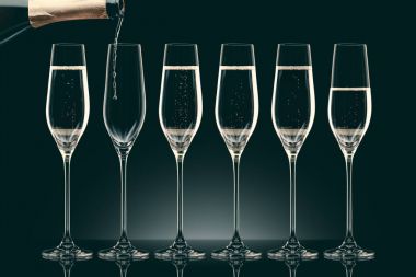 pouring champagne from bottle into six transparent glasses on black clipart
