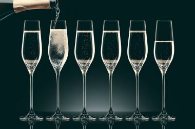 pouring champagne from bottle into six transparent glasses on black clipart