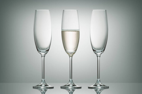 two empty glasses and one glass with champagne on white