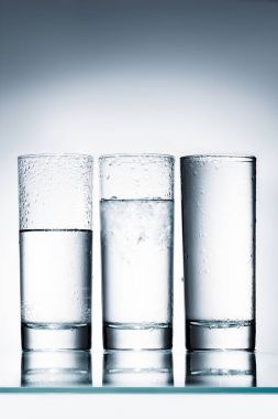 glasses of water in row of different levels on reflective surface clipart