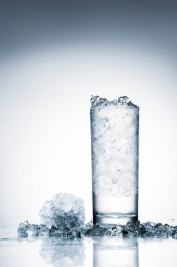 glass of cold water with ice on reflective surface on white  clipart