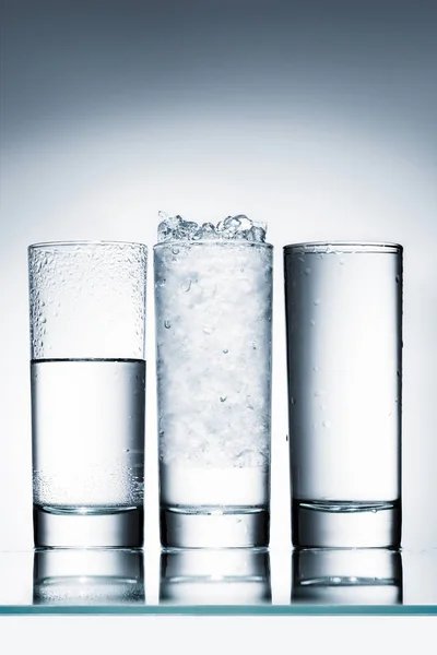 Vasos Agua Fila Uno Con Hielo Sobre Superficie Reflectante —  Fotos de Stock