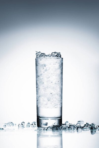стакан холодной воды с дробленым льдом на отражающей поверхности на белом
 