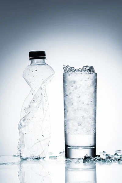 Szklankę Zimnej Wody Lodem Zmięty Plastikowe Butelki Powierzchni Odbijającej Białym — Darmowe zdjęcie stockowe