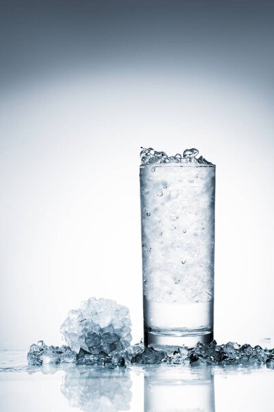 стакан холодной воды со льдом на отражающей поверхности на белом
 