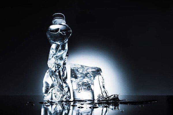 мятая пластиковая бутылка с водой и чашка на темной
 