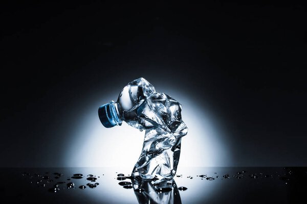 натюрморт со смятой пластиковой бутылкой воды на темной
 