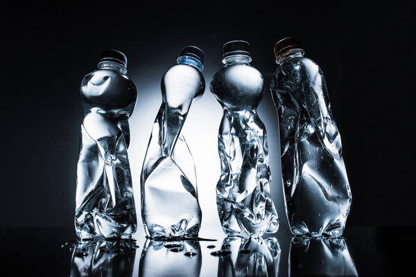 ряд скомканных бутылок с водой в темноте
 
