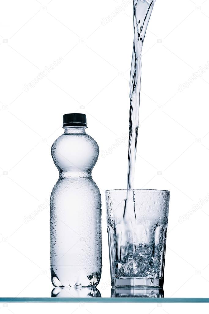 plastic bottle and water pouring into glass isolated on white