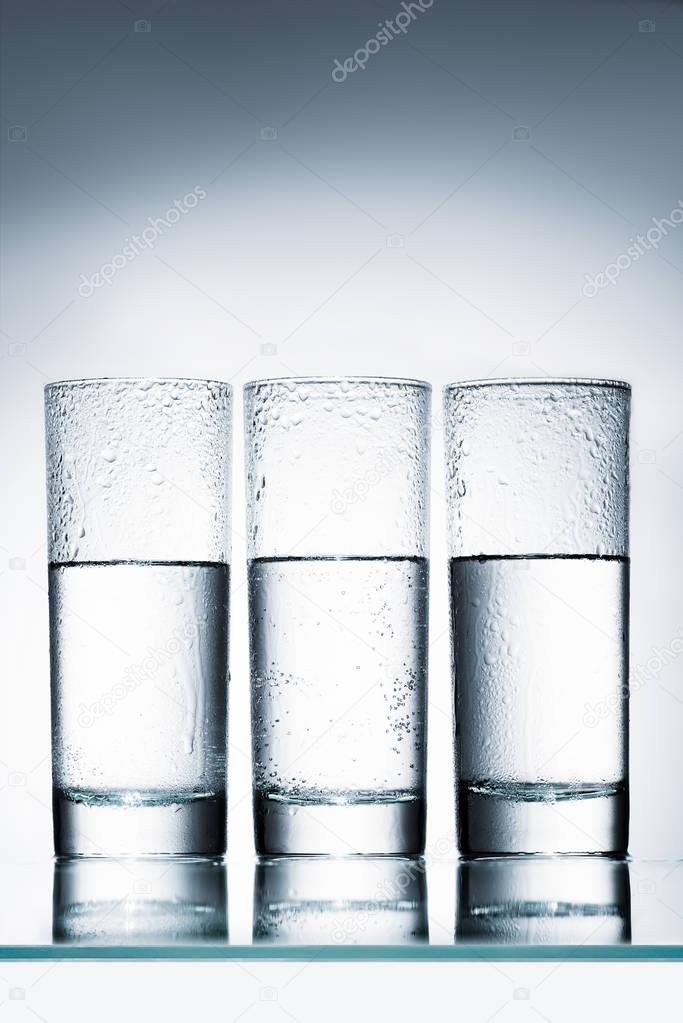 half full glasses of water in row on reflective surface