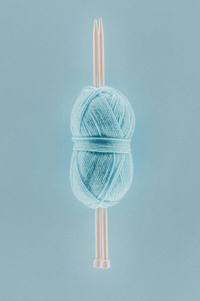 top view of blue knitting yarn ball with knitting needles, isolated on blue