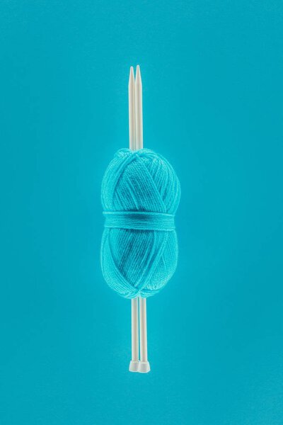 top view of blue knitting yarn ball with knitting needles, isolated on blue