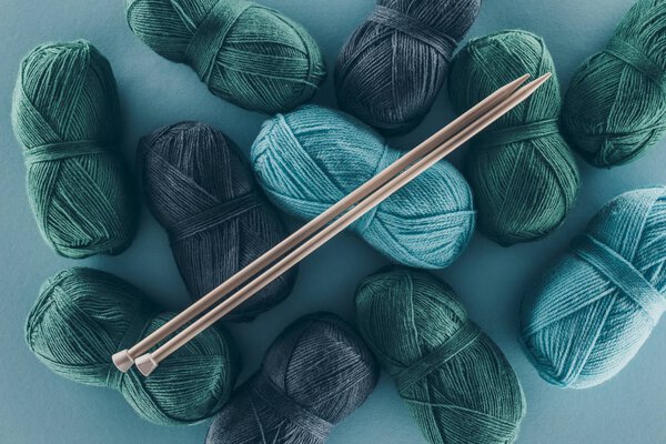 top view of blue and green knitting yarn with knitting needles, isolated on blue
