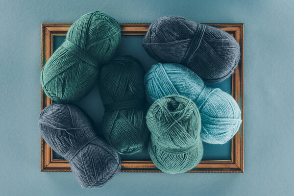 top view of blue and green knitting wool balls on frame, isolated on blue