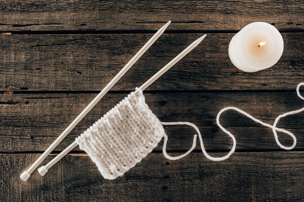 top view of knitting needles with yarn and candle on wooden background