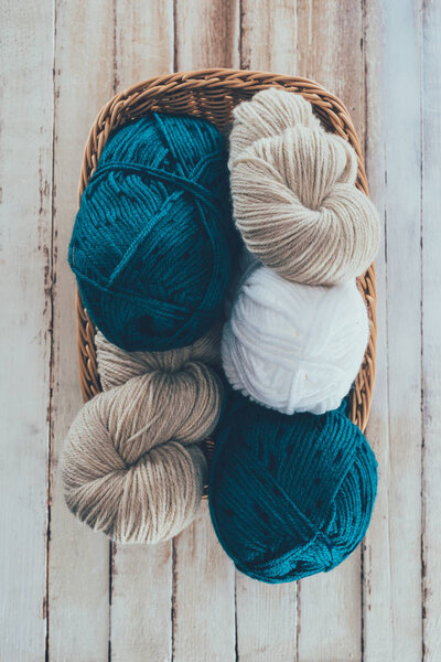 top view of knitting yarn in wicker basket on wooden background