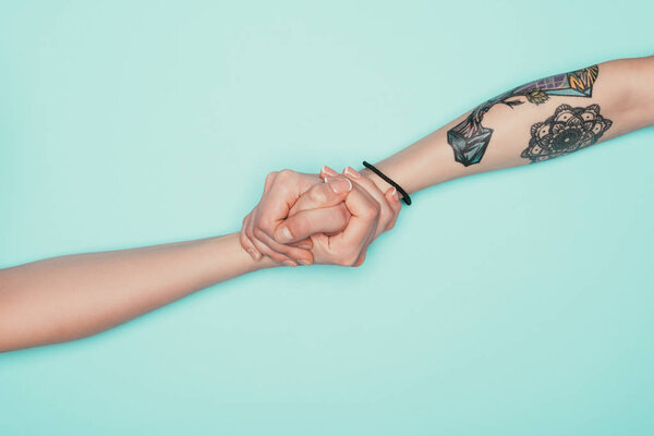 cropped shot of women holding hands isolated on turquoise