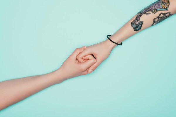 cropped shot of women holding hands isolated on turquoise