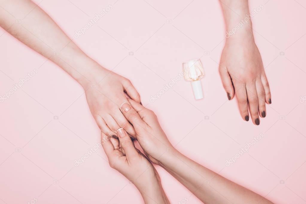 cropped shot of manicurist holdign hand of client isolated on pink