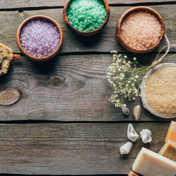 top view of dried flowers and sea salt in wooden bowls on black marble surface with copy space, spa concept