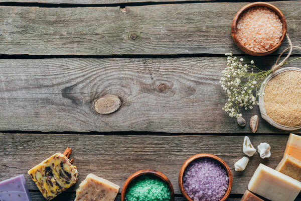 top view of homemade soap and sea salt in wooden bowls on black marble surface with copy space, spa concept