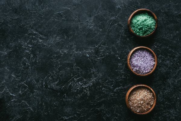 top view of different sea salt in wooden bowls on black marble surface