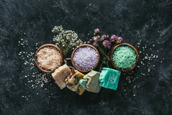 вид сверху на самодельное мыло, сушеные цветы и морскую соль в деревянных чашах на поверхности черного мрамора
