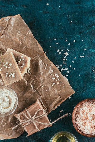 вид сверху на натуральное мыло ручной работы, гималайский соляной и соляной скраб для спа на мятой бумаге на зеленой мраморной поверхности
