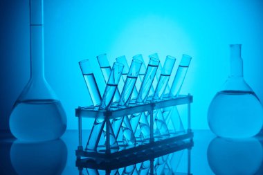 glass tubes with liquid on stand and glass flasks on table on blue clipart