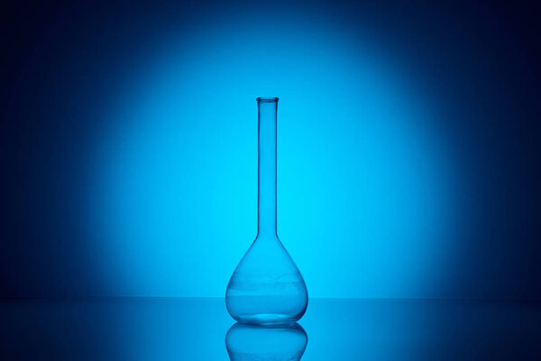one transparent glass flask on reflecting table in laboratory on blue