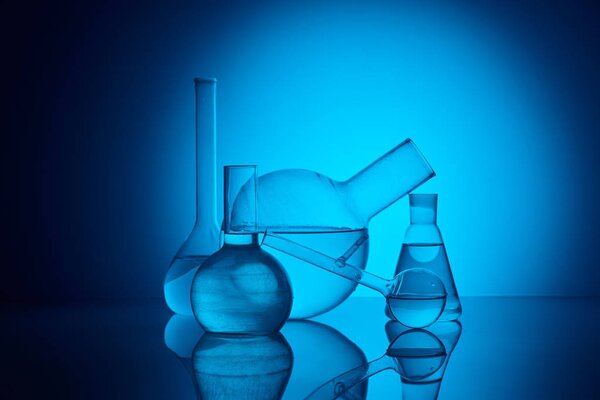 different glass flasks on reflecting table in laboratory on blue