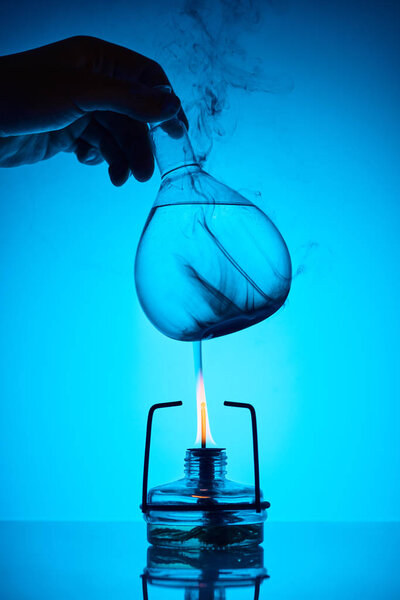 cropped image of chemist warming up substance for analysis on blue