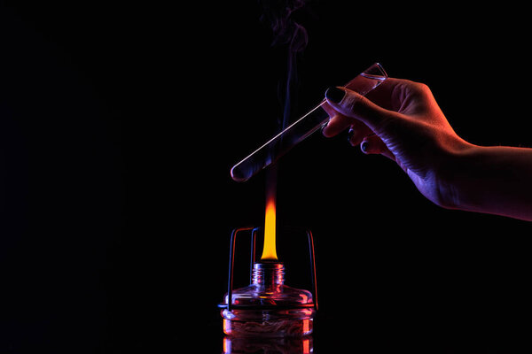 cropped image of chemist warming up tube with liquid on black 