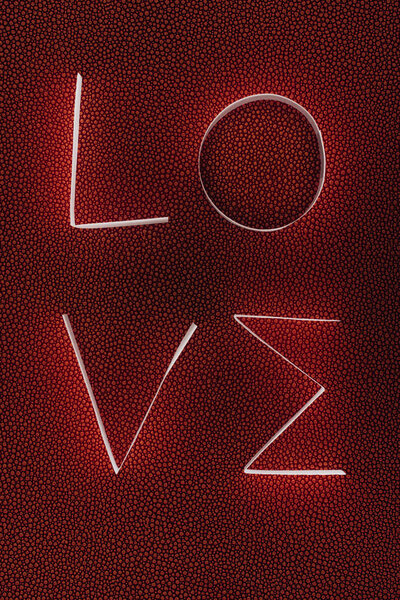 word LOVE made of paper stripes on dark red surface