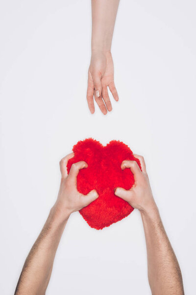 cropped shot of man squeezing red heart pillow while woman reaching for it isolated on white