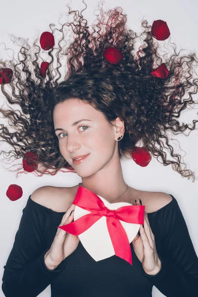 美丽的年轻女子卷曲的头发举行情人节礼物的白色隔离 — 图库照片