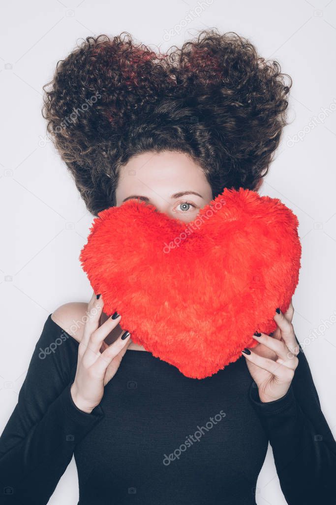 young woman covering face with pillow in shape of heart isolated on white