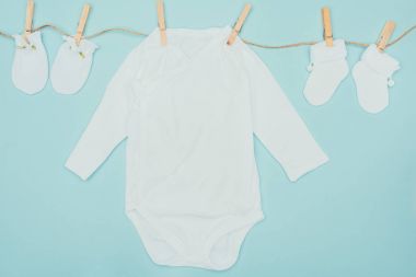top view of baby bodysuits and socks drying on rope isolated on blue clipart