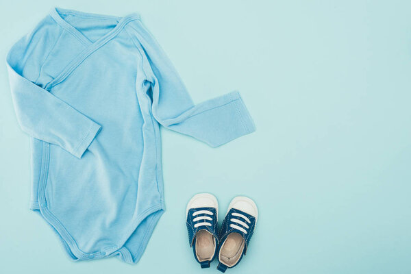 top view of baby bodysuit and shoes isolated on blue