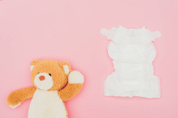 top view of teddy bear and unused diaper isolated on pink