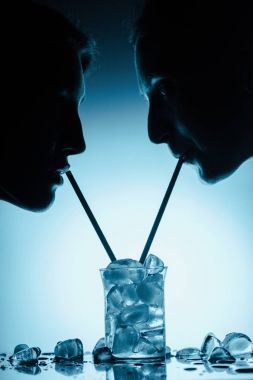 silhouettes of girls drinking cold water with ice cubes from one glass with straws clipart