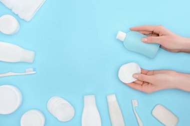 cropped view of woman holding cotton swab and lotion isolated on blue with toothbrushes, soap and cream clipart