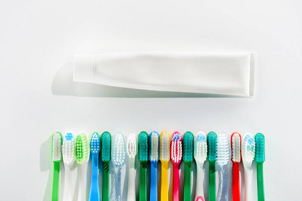 top view of colorful toothbrushes and tube of toothpaste, on white
