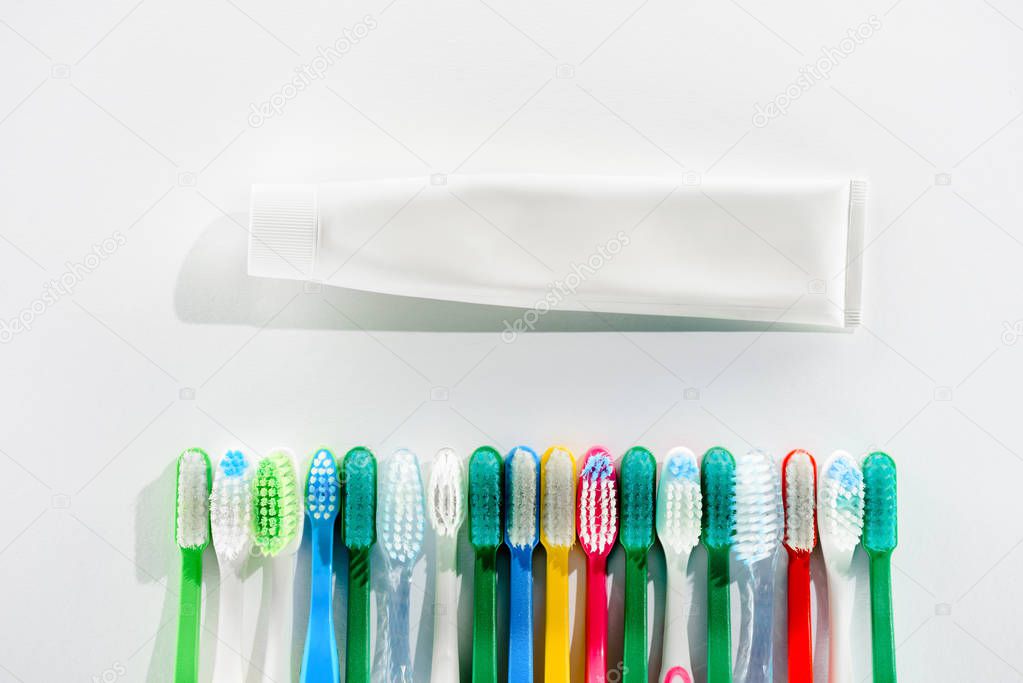 top view of colorful toothbrushes and tube of toothpaste, on white