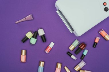 top view of scattered nail polishes and uv lamp isolated on purple clipart