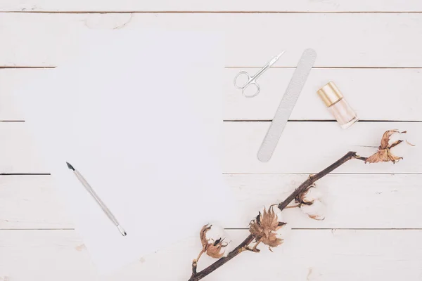 top view of scissors, nail file and nail polish with white paper on wooden table