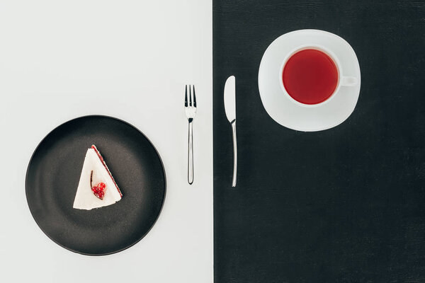 top view of piece of cake on plate, cutlery and cup of tea